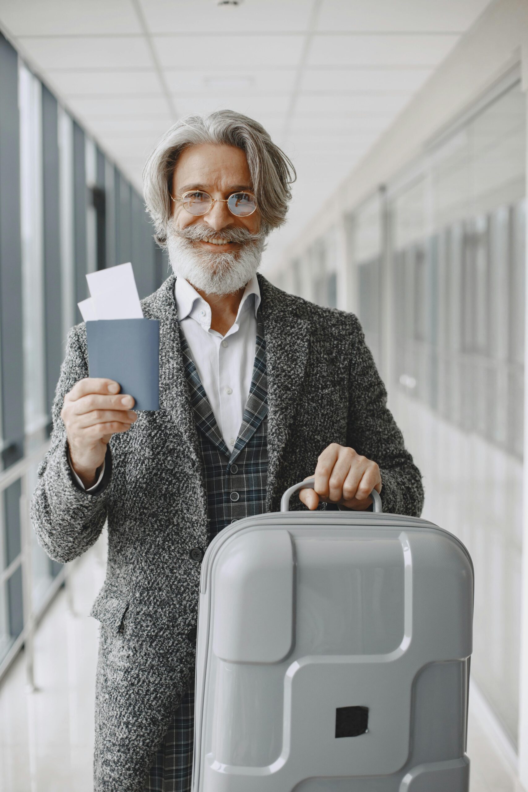 Elderly man in airport holding passport and luggage, smiling confidently at the camera.